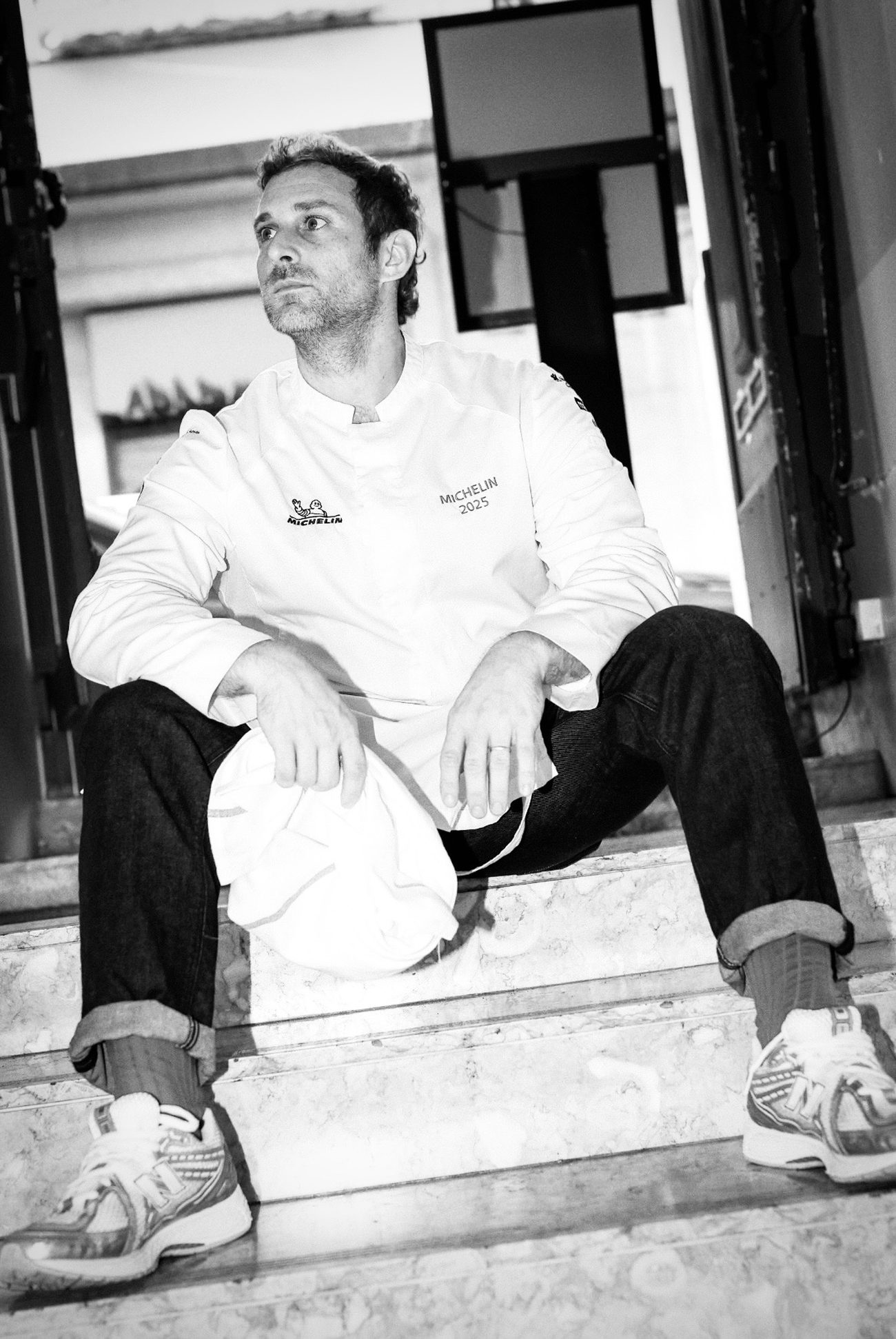 Mattia Stanchieri sitting on marble stairs outside the kitchen in chef whites